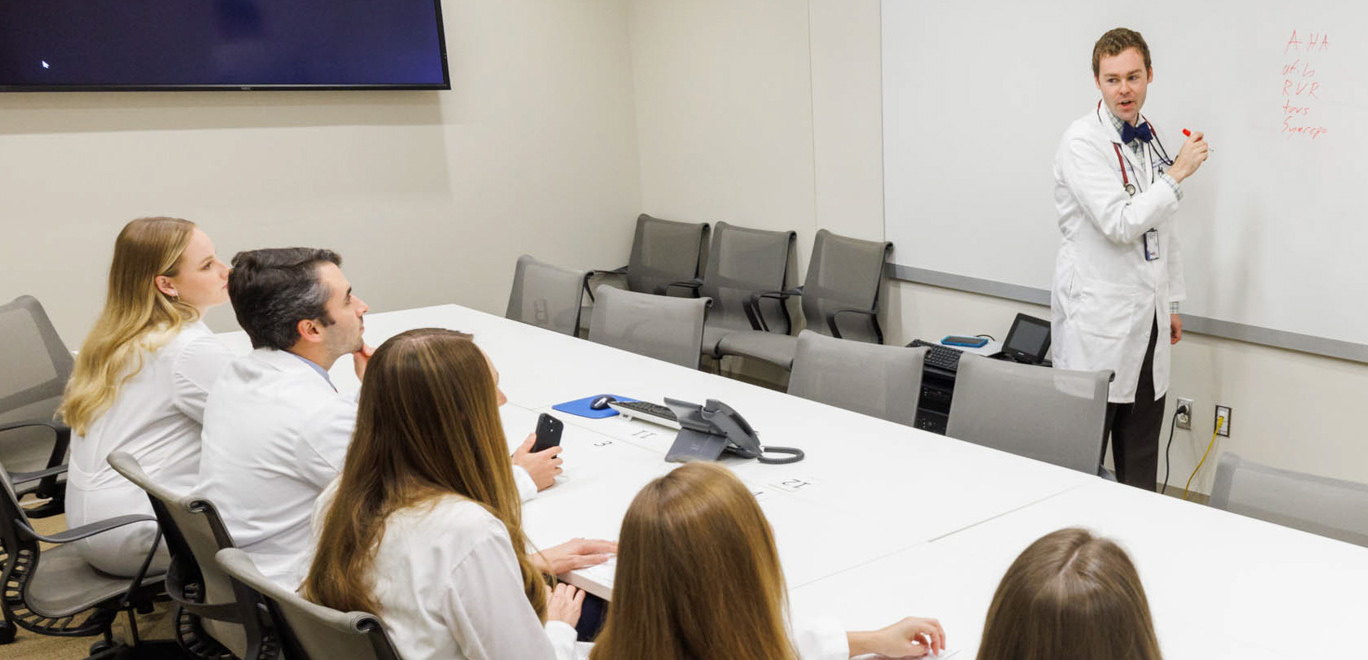 Med-Peds residents sitting in classroom listening to instructor standing in front of the whiteboard.